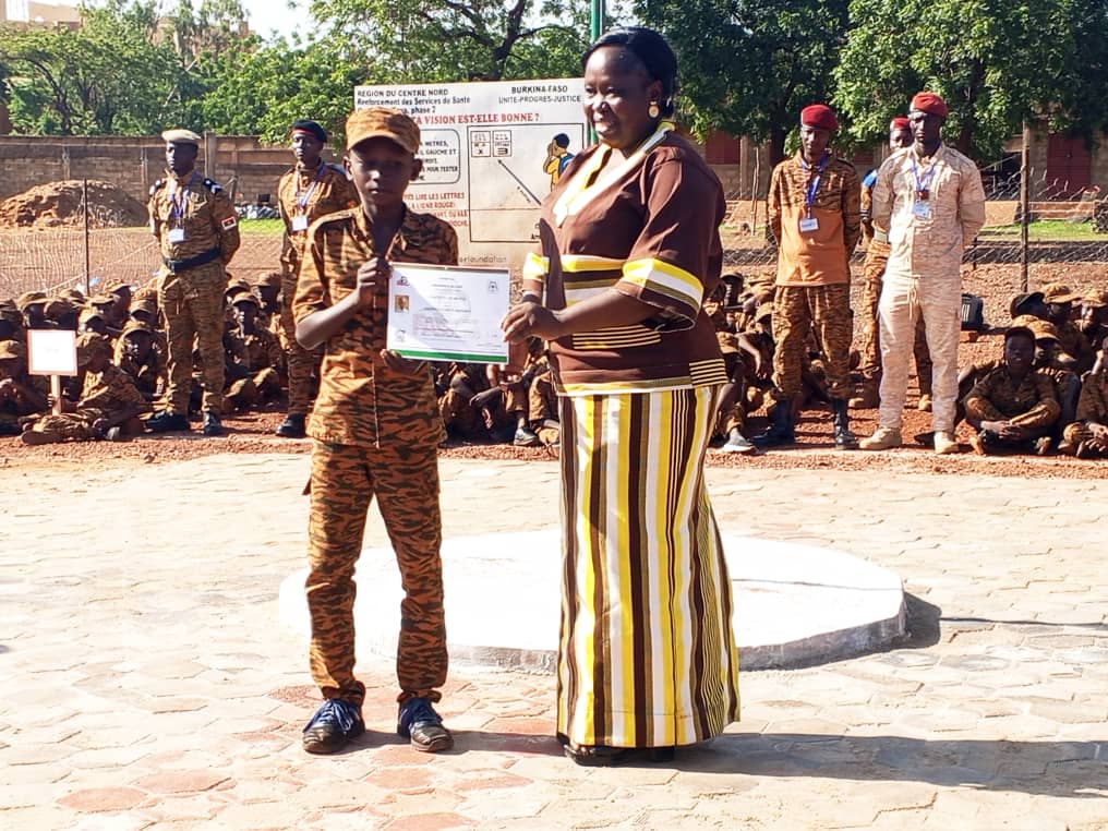 La Camarade Bernadette ADENYO/SERME , Gouverneur par intérim de la région des Koulsé remettant une attestation de participation à un campeur à la cérémonie de clôture le 20 août 2026 du camp vacances Faso Mêbo des Koulsé à Kaya